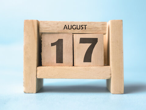 A wooden block calendar for August 17th on a light blue background.