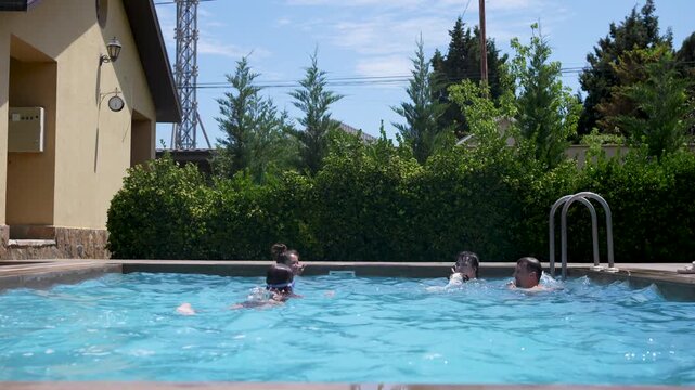 Happy family swimming, splashing water, and having fun in an outdoor pool while a Jack Russell terrier dog runs along the poolside on a sunny day