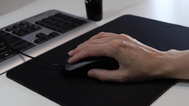 Person Using Computer Mouse on Black Pad Beside Keyboard at White Desk