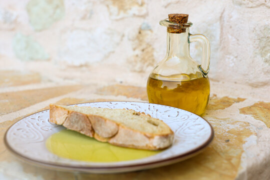 A slice of rustic bread rests in golden olive oil beside a glass bottle in Greece, highlighting the simplicity and authenticity of Mediterranean cuisine.