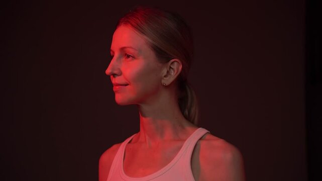 Woman at black background in red light looking at camera and smiling. video footage