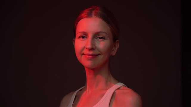 Smiling Woman at black background in red light relaxed  looking at camera. video footage