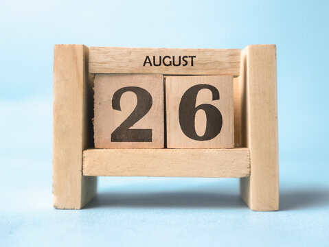 A wooden block calendar for August 26th on a light blue background.