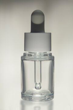Minimalist clear glass dropper bottle with a white cap isolated on a neutral background. Blank cosmetic packaging mockup suitable for skincare, facial serum, essential oil, beauty branding, product pr