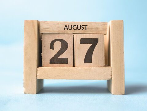 A wooden block calendar for August 27th on a light blue background.