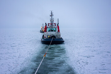 Obraz premium Tugboat Towing Rope Through Ice-Covered Frozen Sea, Maritime Winter Icebreaking Operation. Winter Maritime Logistics and Navigation in Frozen Cold Water, Marine Transportation