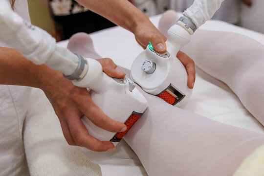Professional body contouring and cellulite treatment on female legs using specialized vacuum roller massage device in a modern beauty spa clinic.