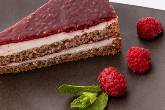 Delicious raspberry layer cake slice with fresh berries on a dark plate. Gourmet fruit dessert for bakery and cafe menus