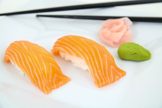 Fresh salmon nigiri sushi with wasabi and pickled ginger on a white plate. Traditional Japanese food.