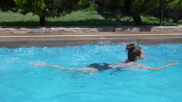 Happy young woman enjoying a refreshing swim in a clear blue outdoor pool at a private villa during summer vacation