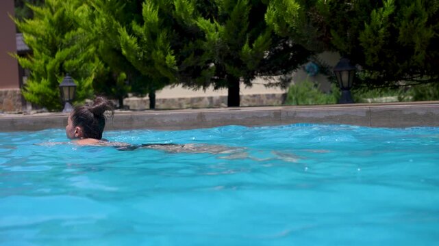 Happy young woman enjoying a refreshing swim in a clear blue outdoor pool at a private villa during summer vacation