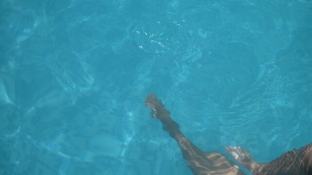 Top view of woman legs swimming underwater in clear blue pool