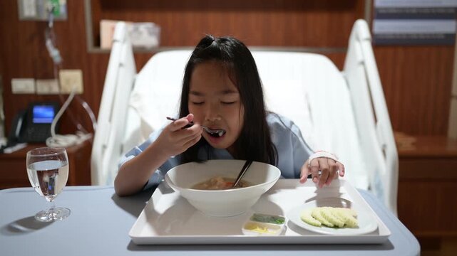 Young patient eats a meal while sitting in a hospital bed during recovery. Concept of pediatric healthcare, hospitalization, nutrition, patient care, treatment, and healing.