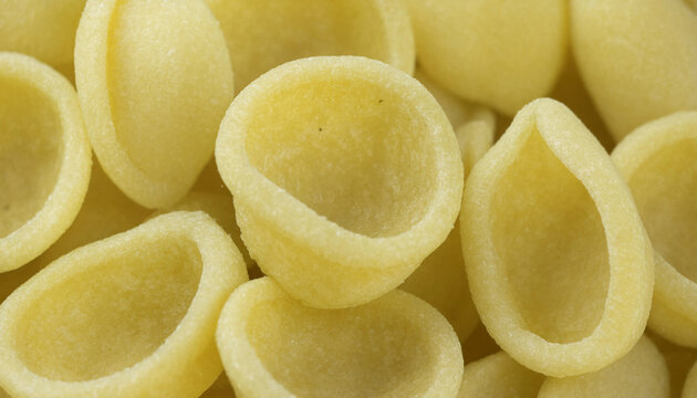 A close-up top-down view of a pile of raw orecchiette pasta shapes, showing the smooth, pale yellow dough texture and uniform curved forms