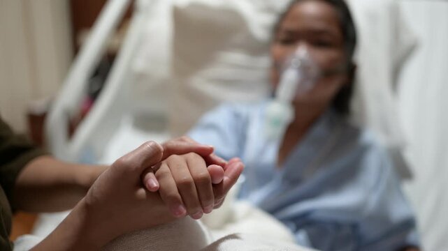 A concerned mother holds her sick child's hand while the child receives oxygen therapy in a hospital bed. Family support, pediatric healthcare, compassion, medical treatment, and hope for recovery.