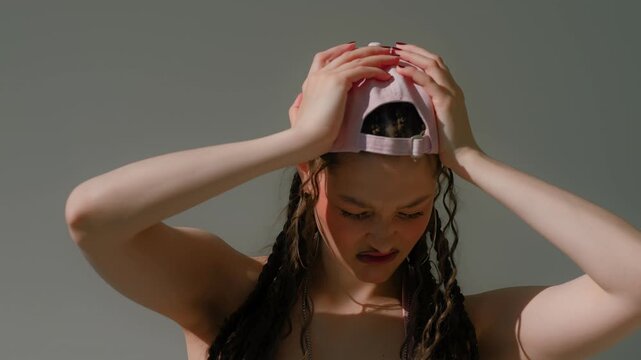 Woman with braided hair and baseball cap holding head up under strong sun, tense thoughtful pose cap
