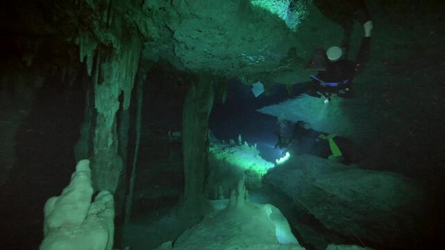 Equipped divers move through a low underwater chamber among hanging formations at Cenote Carwash, Quintana Roo, Mexico.