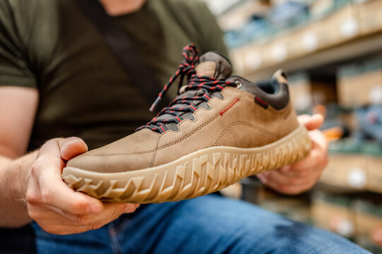 Person holds brown sneaker with rugged rubber sole inside shop during daytime retail visit