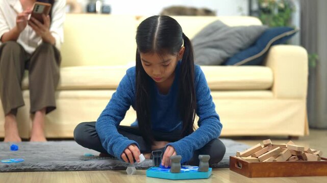 Girl Playing with Wooden Blocks on Living Room Floor While Mother Uses Smartphone at Home