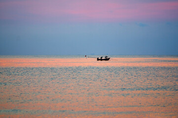 Fototapeta premium Small fishing boat floating on calm ocean water during a vivid colorful sunset horizon.