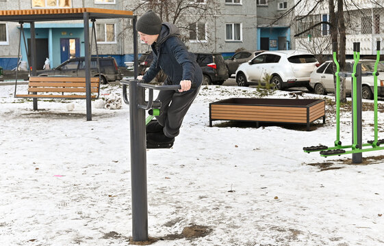 Workout of elderly man on winter outdoor gym. Mature man making physical exercises in spite of snowstorm.