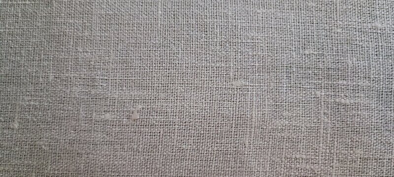 Top down close up of light gray beige linen or cotton with a visible coarse weave of horizontal and vertical threads.