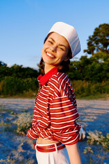 Obraz premium Smiling woman outdoor lifestyle portrait in a striped shirt and beret. The joyful girl poses on a beach at sunset. Concept of summer leisure, happiness, and authentic style.