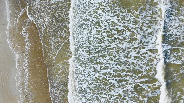 Aerial top down view of breaking wave lines and foam patterns along sandy shoreline. Abstract sea texture background