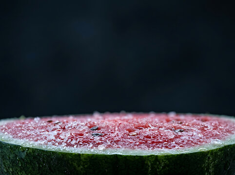Close-up macro shot of a fresh, juicy watermelon slice with water droplets on red flesh and green rind against a dark background