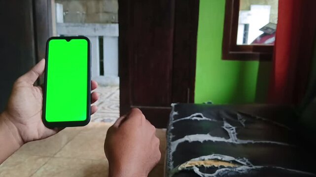 Person holding smartphone with green screen display. User interacting with mobile device for video editing or app demonstration.