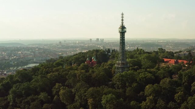 Petrin lookout tower stands in green forest park in early morning Prague. Steel observation structure forms tourist attraction. Historic cityscape represents european travel destination.