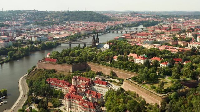 Historic Vysehrad fortress overlooks Vltava river and city bridges in Prague. European architectural landmark serves as popular tourist attraction. Scenic urban landscape represents travel.