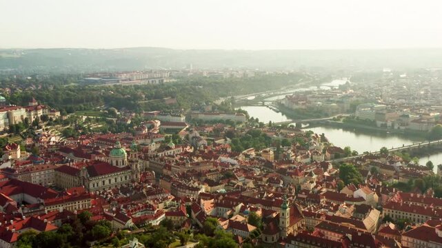 Early morning sun illuminates Prague cityscape and Vltava river bridges. Historic European architecture showcases red tiled roofs. Soft morning light creates peaceful travel destination.