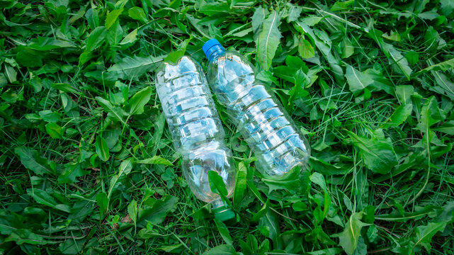 Two empty clear plastic bottles discarded on green grass, environmental pollution and recycling concept