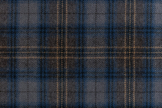 Flat lay of a grey wool fabric with a blue and tan tartan check overlay, well suited for menswear, upholstery and autumn fashion themes.