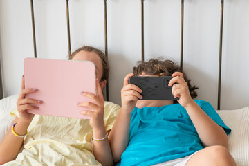 Siblings are intensely focusing on their tablet and smartphone, highlighting concepts of digital engagement and screen time for youth © Nuria Gonzalez Sanch