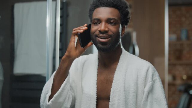 Cheerful African American man friendly talking mobile phone looking at mirror reflection at home bathroom carefree ethnic guy talk smartphone enjoying conversation at morning hygiene beauty routine