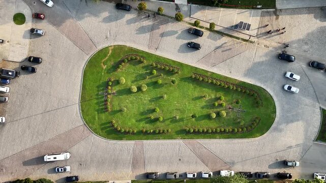 Aerial top down view of urban car parking lot with vehicles moving and pedestrians walking, showing a green space traffic island and city transportation concept