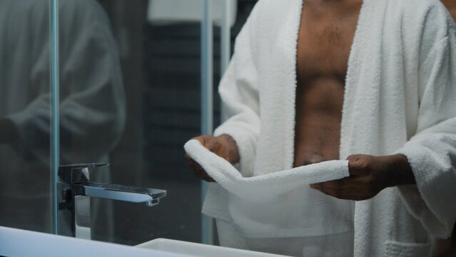 Cropped view unrecognizable African American ethnic man holding bath white towel preparing for wiping in bathroom guy wipe after washing at morning home male refreshing hygiene dermatology procedure