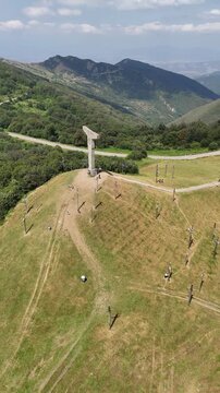 Drone orbiting around the majestic cross monument on mount didgori, revealing the stunning georgian landscape with rolling green hills, lush forests, and a clear blue sky