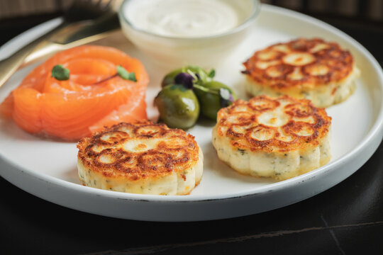Savory Syrniki with Smoked Salmon, Olives and Sour Cream on White Plate