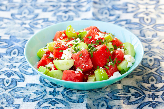 Watermelon salad with cucumber and feta cheese in blue bowl on blue patterned tablecloth. Close up.