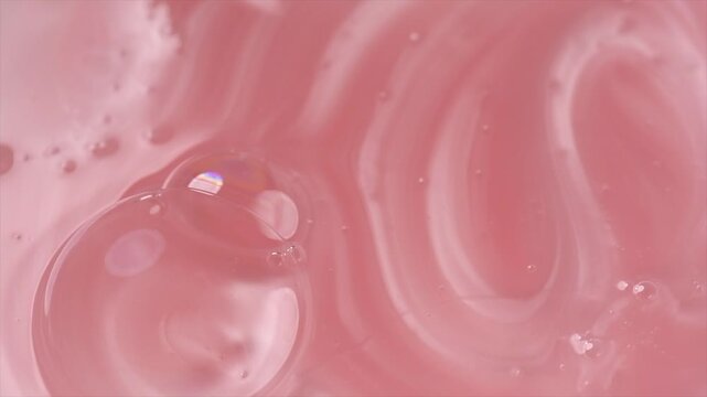 Liquid pink shampoo texture background, washing gel, soap. Pearlescent surface of liquid pink fluid, body care cosmetic, soap backdrop with bubbles top view, from above, rotating 