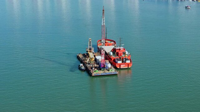 Aerial view of dredging equipment in coastal sea water near urban shoreline. Seabed excavation and marine maintenance activity