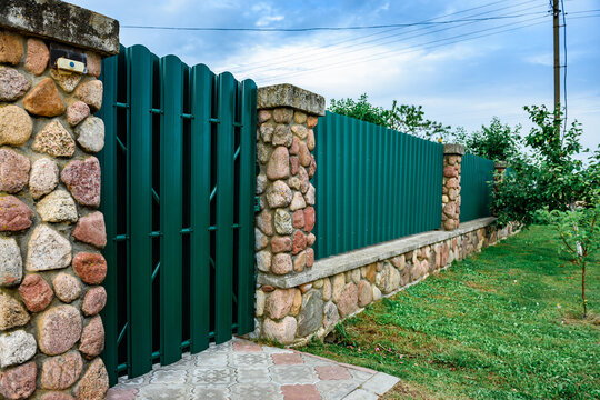 Close up of green metal picket fence enclosing a private cottage. Property boundary, house security and territory concept.
