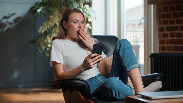 Amazed surprised Caucasian middle-aged woman using mobile phone reading amazing news surprise wondering emotion at home adult female browsing smartphone opening mouth feeling disbelief in apartment