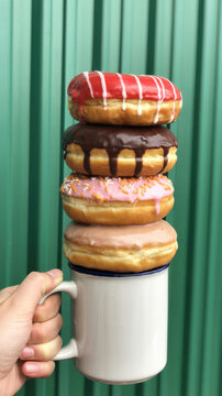 Stack of four donuts held by hand on white mug with green background.