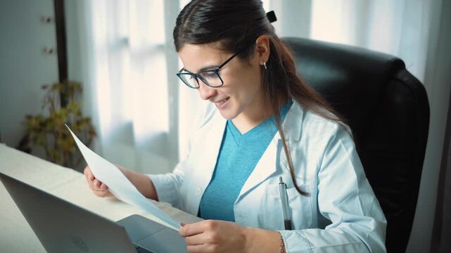Young Hispanic female nurse in a medical office entering medical data into her laptop, representing healthcare technology, clinical documentation, patient care, and modern medical work.
