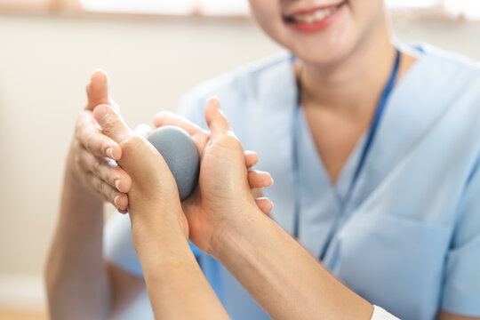 Close up of a physical therapist guiding a patient through hand exercise using a grey therapy ball for rehabilitation, occupational recovery and healthcare concept.