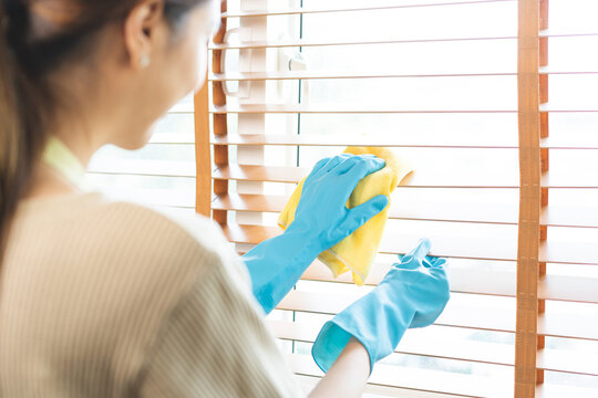 Happy housewife asian young woman worker wear apron and rubber gloves at home, cleaning interior work in house, holding wipe, rag cloth dust to clean window blinds. Cleaner and chore service concept.